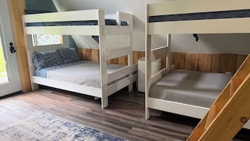 A room with two bunk beds, a wooden floor, a patterned rug, and a door with a window.