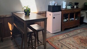 Een eethoek met een houten tafel en banken, een kleine koelkast, en een decoratief kunstwerk aan de muur.
