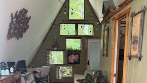 Een knus zolderkamertje met een schuine kap, een houten bureau, een groene fauteuil en een kamerbreed tapijt met een patroon.