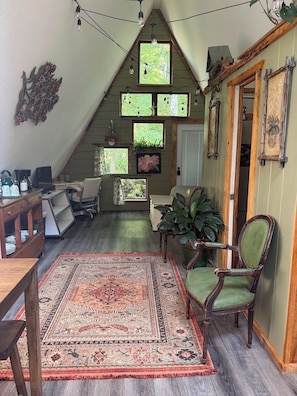 A cozy attic room with a sloped ceiling, a wooden desk, a green armchair, and a patterned rug.