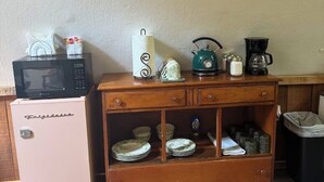 Een kitchenette met een roze koelkast, een magnetron, een waterkoker en een koffiezetapparaat op een houten aanrecht.