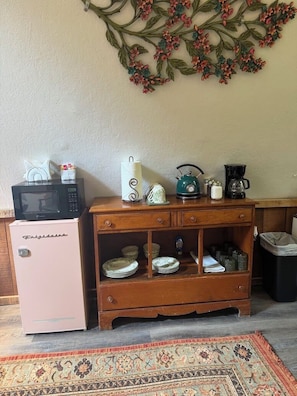 A kitchenette with a pink refrigerator, a microwave, a kettle, and a coffee maker on a wooden counter.