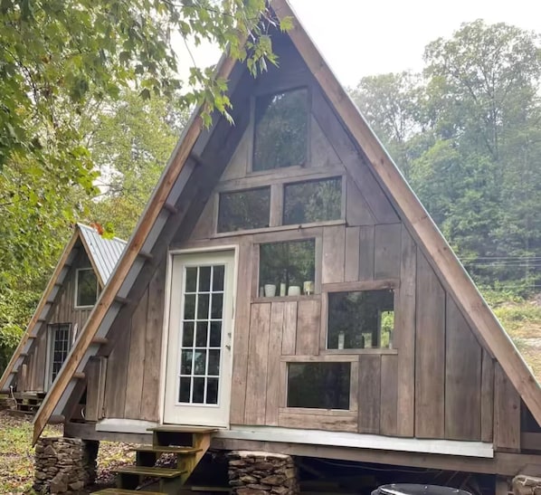 Une cabane en bois avec un toit triangulaire, une porte d’entrée et plusieurs fenêtres.