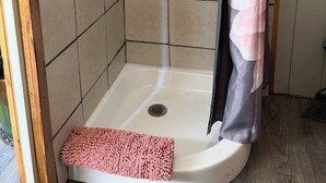 Een douche met betegelde wand, een douchegordijn en een roze badmat.
