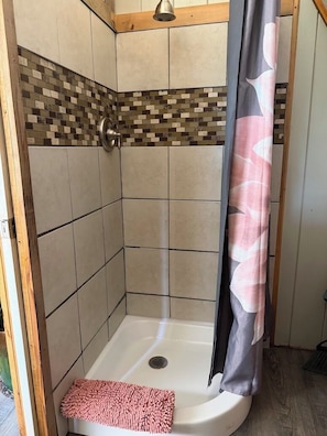 A shower with a tiled wall, a shower curtain, and a pink bath mat.