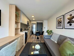 A modern living room with a sofa, a coffee table, and a dining area with chairs and a table. - 2BR Andes View - Parking, Pool & Metro (Santiago)