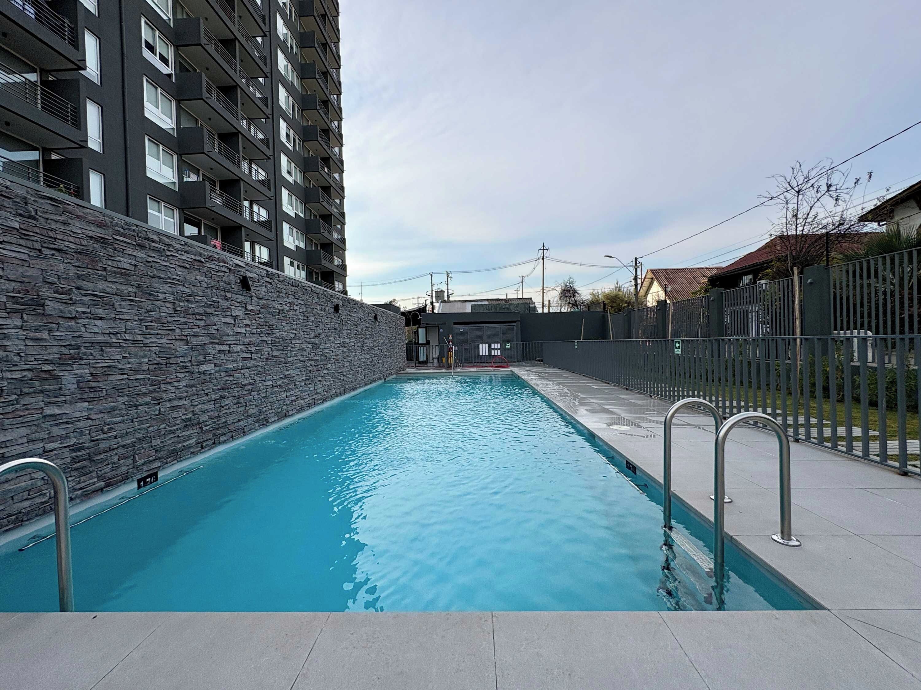 Una piscina con un muro de piedra en un lado y una valla metálica en el otro.