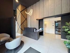 Un'area di accoglienza con scrivania della reception, una moderna poltrona, una pianta in vaso e una scala con pannelli in legno.