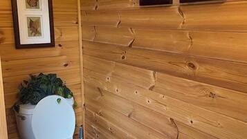 Een compacte houten badkamer met een toilet, een klein wastafeltje en ingelijste foto's aan de wand.