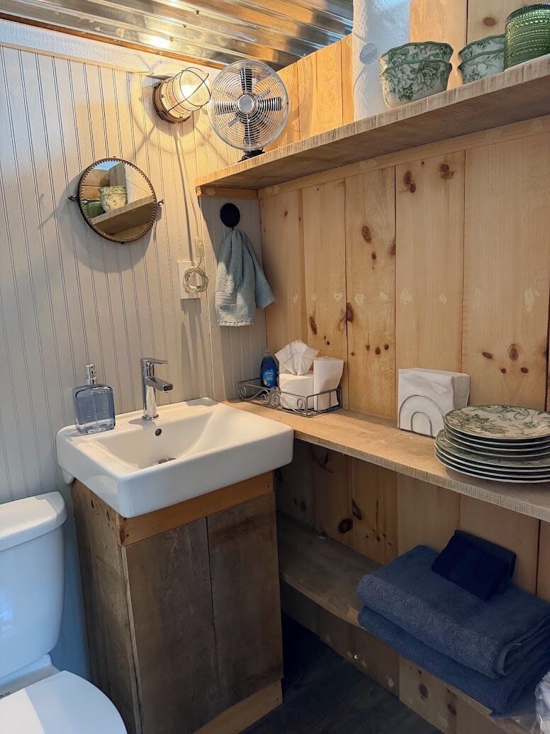A bathroom with a wooden vanity, a sink, a mirror, a towel rack, and a fan.
