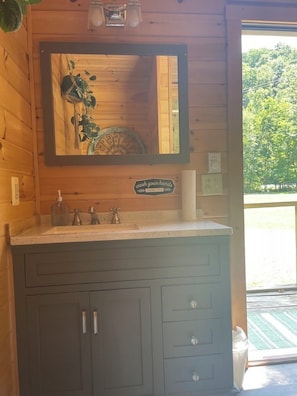 A wooden cabin interior with a wooden vanity, a mirror, a sink, and a sign that reads 'wash your hands.'