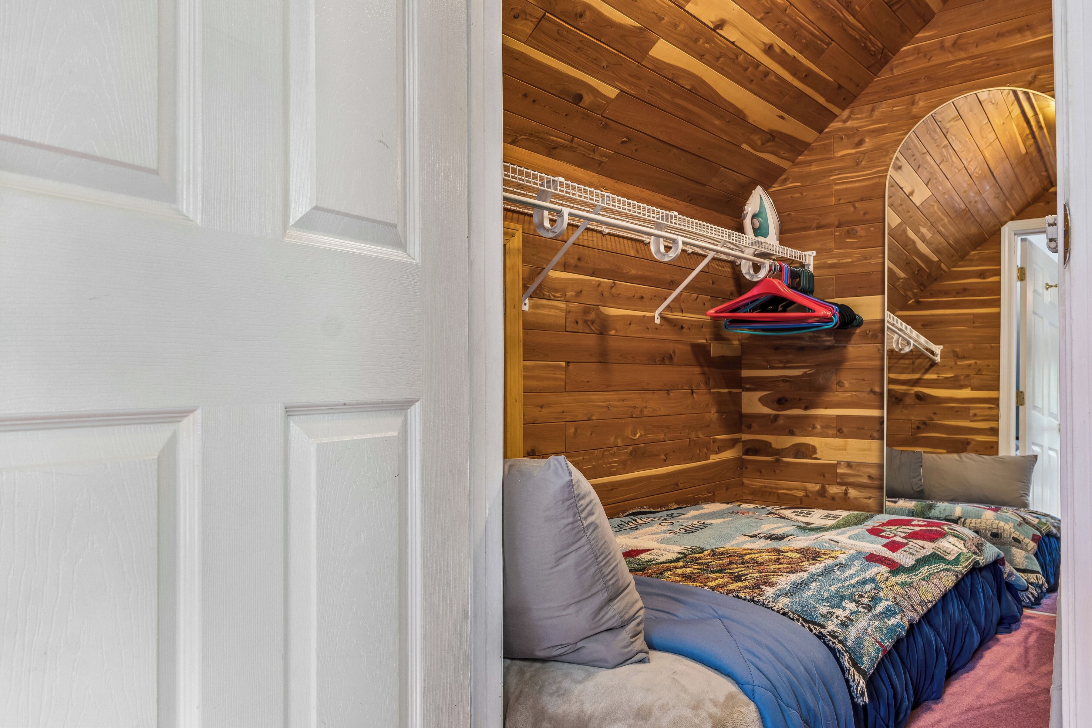 A wooden interior with a bed, a hanging clothes rack, and a door.