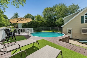Un jardin avec une piscine, des chaises longues et un parasol.