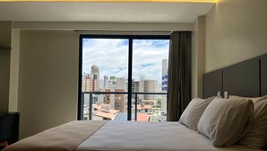 Habitación de hotel con una cama grande, vistas de la ciudad a través de un ventanal amplio y un diseño moderno.