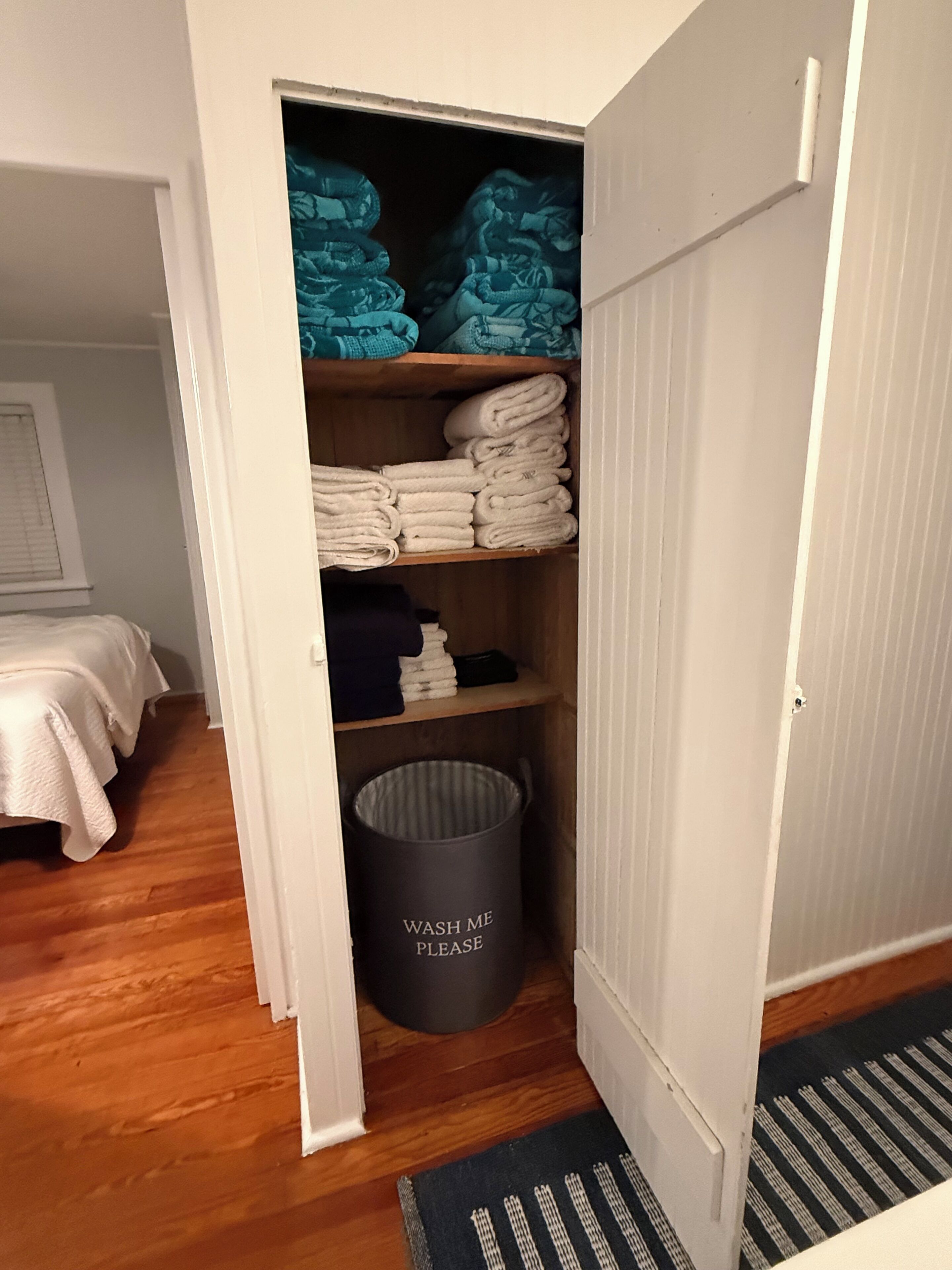 Une chambre avec un lit, une armoire contenant des serviettes pliées et une poubelle munie d’une étiquette.