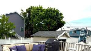 A covered outdoor seating area with a wicker sofa, a small table, and a grill.