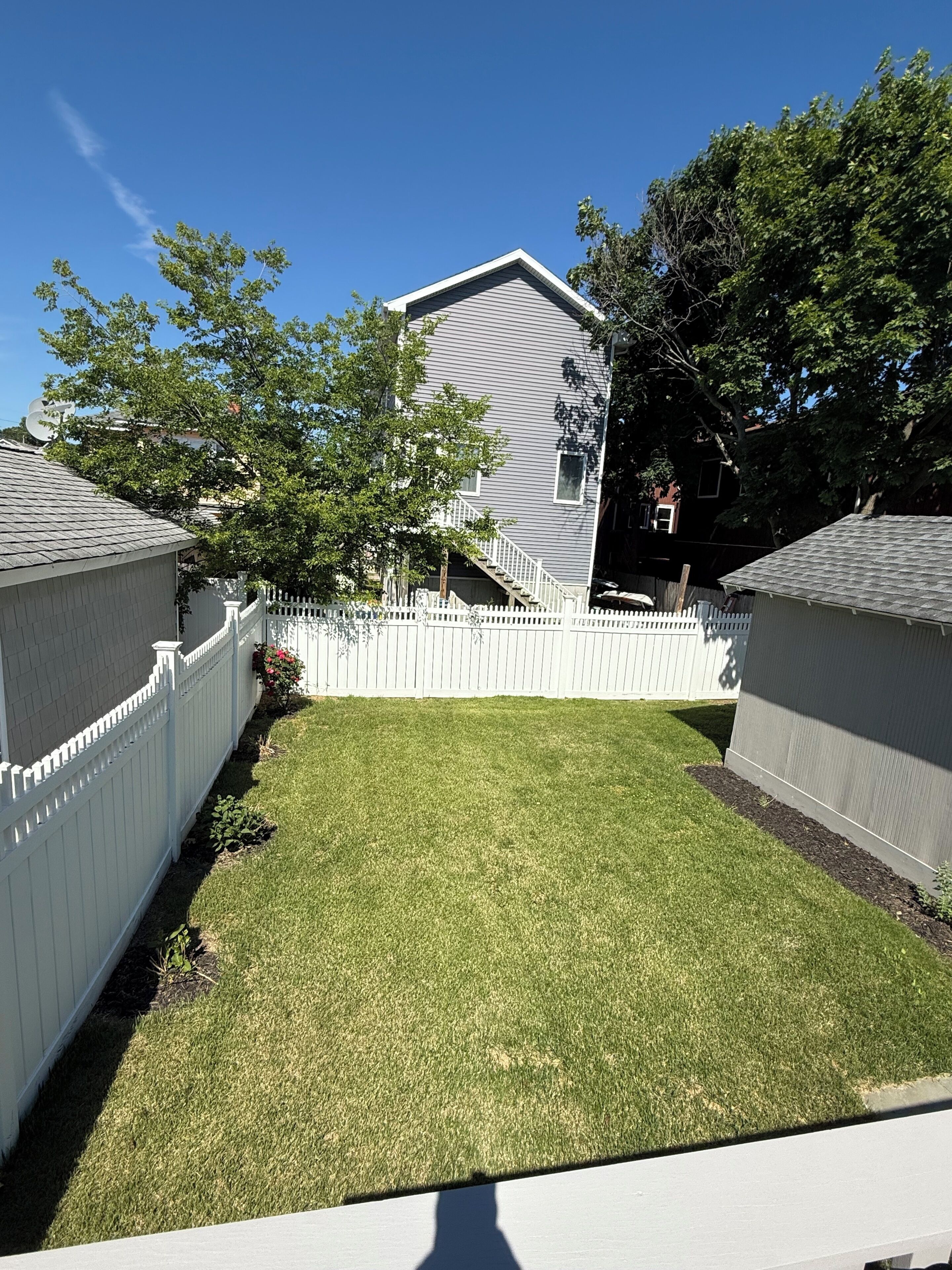 A residential backyard with a white picket fence, a well-maintained lawn, and a house with a grey exterior.