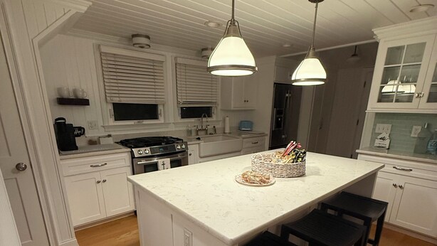 A kitchen with white cabinetry, a central island with bar stools, a stove, and pendant lighting.