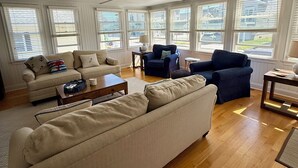 A spacious living room with a high ceiling, large windows, and a variety of seating options including a sofa, armchairs, and a coffee table.