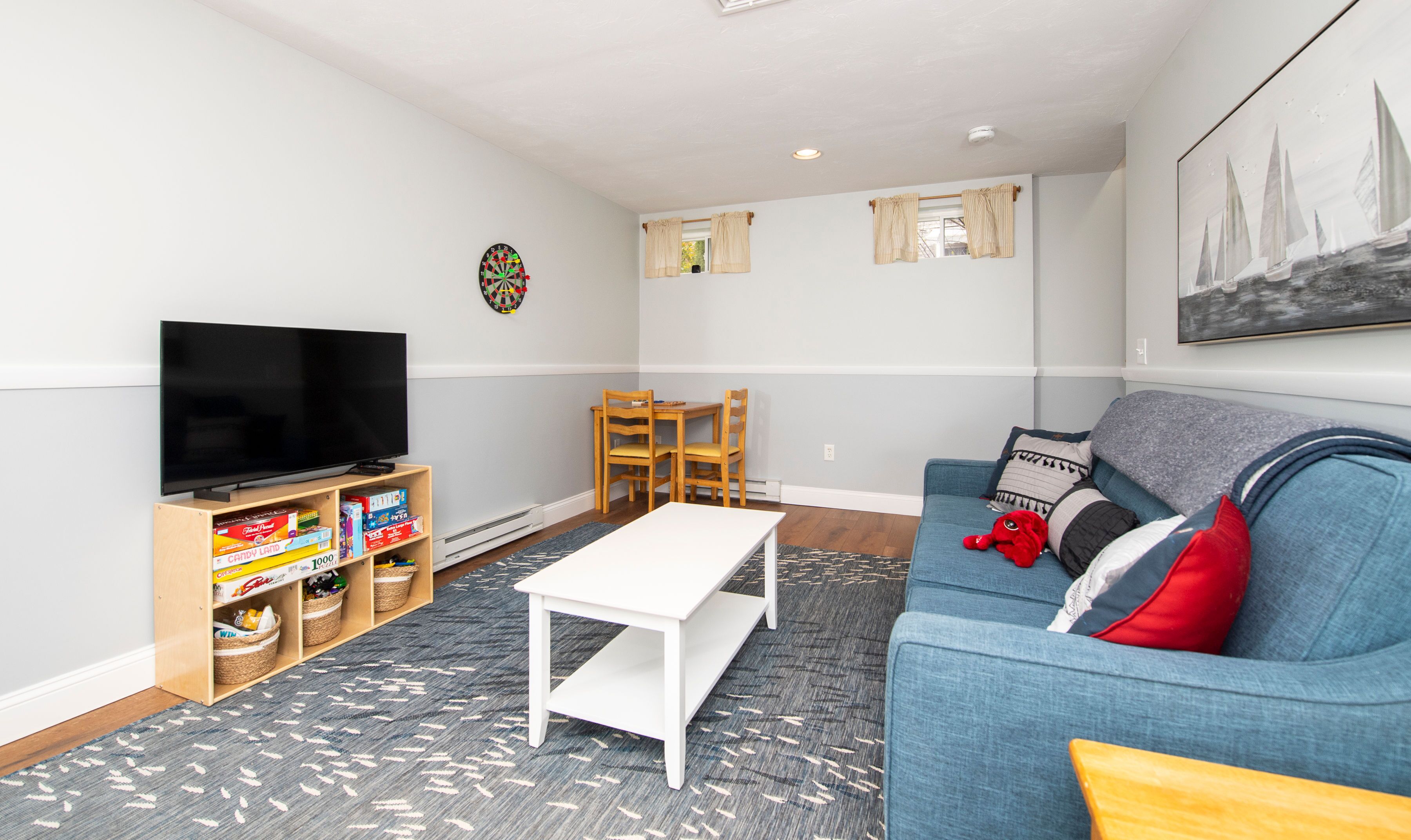 A living room with a TV, a dartboard, a bookshelf, a dining table, and a couch.
