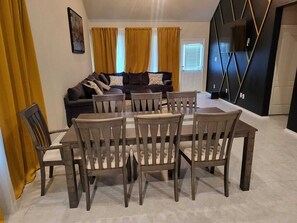 A dining area with a round table and six chairs, a sofa with cushions, and a TV mounted on the wall. - Spacious 4-bedroom house in charming Richmond with AC (Richmond)