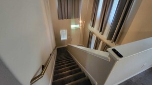 Eine Treppe mit Geländer, ein Fenster mit Jalousien und eine Tür am oberen Ende.