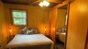 Ein Zimmer mit Holzboden, einem Bett, zwei Nachttischlampen, einem Fenster und einem Spiegel.