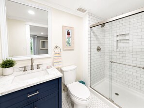Ein Badezimmer mit Toilette in Weiß, einer Dusche mit Glastür, einem мрамор Waschbecken und einem blauen Schrank.