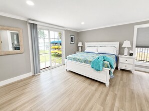 Ein Schlafzimmer mit einem großen Bett, einem Nachttisch, einem Spiegel und einer Schiebetür zu einem Außenbereich.