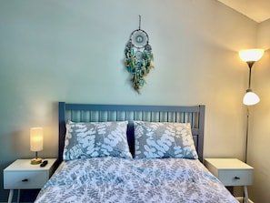 A bedroom with a bed, two bedside tables, a wall-mounted dreamcatcher, and two wall-mounted lamps.