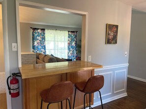 A kitchen with a wooden island, two bar stools, a fire extinguisher, and a painting on the wall.