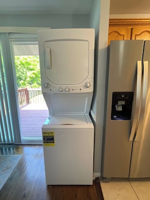 A compact kitchen with a built-in washer and dryer, a stainless steel refrigerator, and a sliding glass door leading to an outdoor area.