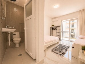 Et moderne badeværelse med bruser, håndvask, toilet og en dør til en balkon.