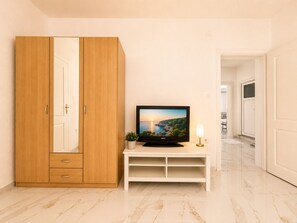 Ein Zimmer mit einem Holzschrank, einem Fernseher auf einem weißen Schrank und einer kleinen Pflanze sowie einer Lampe.