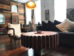 Un salon rustique avec une table basse ronde en bois, un fauteuil ancien, un canapé et une grande fenêtre.