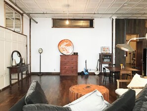 Une pièce avec un plancher en bois, un canapé, une table basse, une commode, une guitare et un tableau accroché au mur.