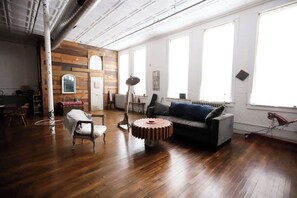 Une pièce spacieuse avec un plancher en bois, un canapé, un fauteuil, une table et un radiateur.