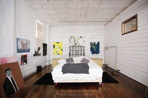 Une chambre à coucher avec un lit, des œuvres d’art accrochées aux murs, un plancher en bois et une fenêtre.