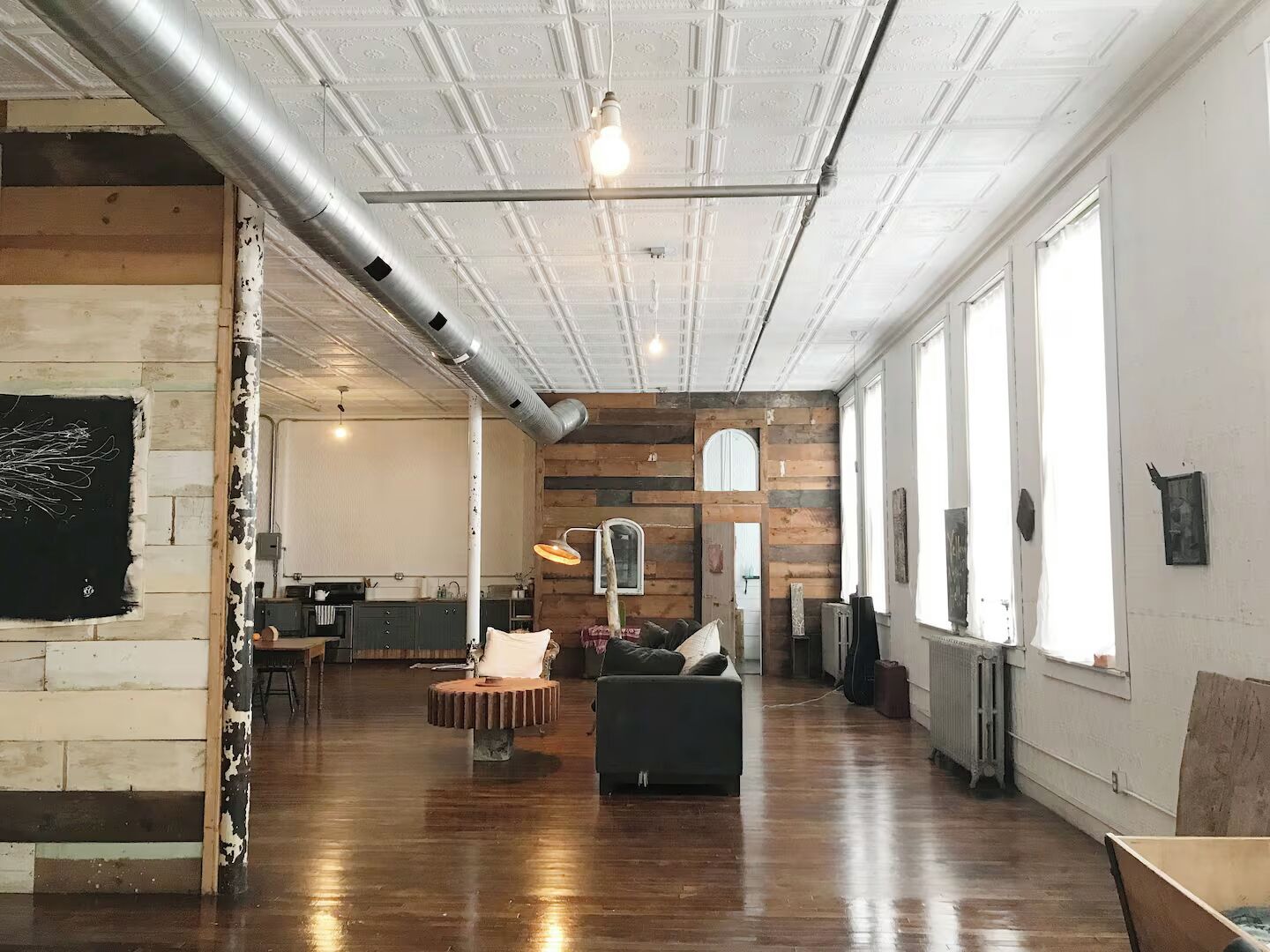 Una habitación amplia con techo alto, conductos expuestos, un ventanal grande, un sofá y una mesa.