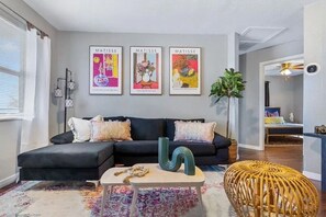 A modern living room with a black sofa, a coffee table, and three framed artworks on the wall. - 15 mins to TPA, Fire pit & Pullout Couch (Tampa)