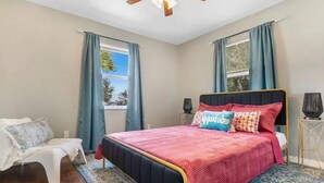 Un dormitorio con cama, una silla, una mesita de noche y una ventana con cortinas.
