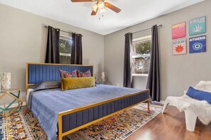 A bedroom with a bed, a ceiling fan, a window with curtains, and wall art. - 15 mins to TPA, Fire pit & Pullout Couch (Tampa)