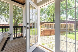 A covered outdoor area with a wooden deck, a bench, and a view of a backyard with a wooden fence and trees. - The Northview Nook- Dog-Friendly Nashville Retreat (Nashville)