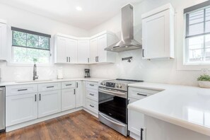 A modern kitchen with white cabinetry, a stainless steel range hood, and a built-in oven. - The Northview Nook- Dog-Friendly Nashville Retreat (Nashville)