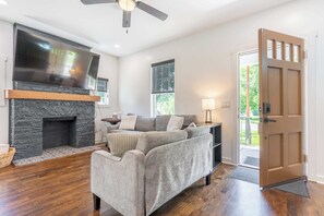 Un salon avec une cheminée, un téléviseur à écran plat, un canapé et une porte donnant sur l’extérieur.