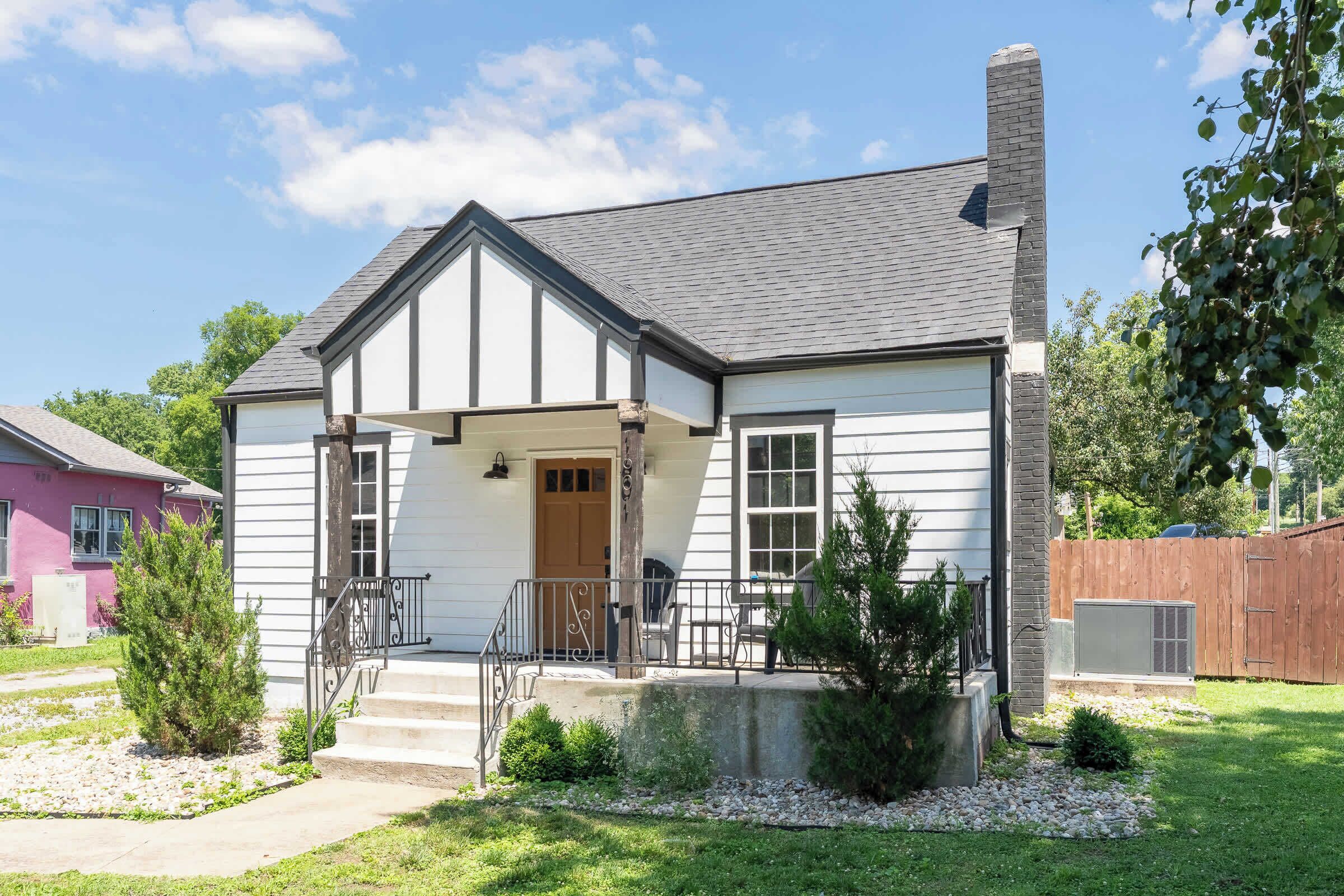 A single-story house with a front porch, a chimney, and a small front yard with a tree and a gravel path.