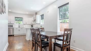 A modern kitchen with white cabinets, a dining table with chairs, and a large window providing natural light.