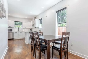 A modern kitchen with white cabinets, a dining table with chairs, and a large window providing natural light. - The Northview Nook- Dog-Friendly Nashville Retreat (Nashville)