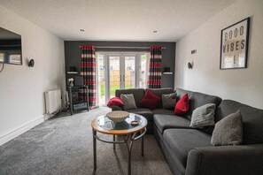 Ein Wohnzimmer mit grauem Sofa, einem Glastisch und einem roten Kissen.