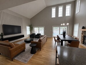 A spacious living room with a flat-screen TV, leather sofas, a dining table, and a stone fireplace. - Dockside Retreat- Riverfront Near Lake Michigan (St. Joseph)